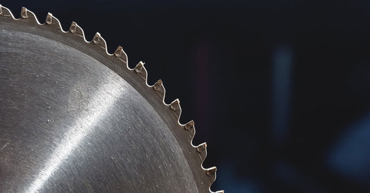 A sharp toothed blade made of metal stands straight with light glinting off of it in front of a dark background.