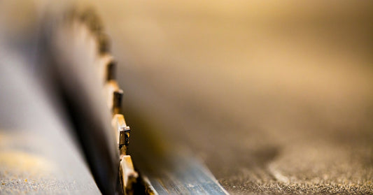 A closeup of a saw blade sticking out of a work table. The saw blade is noticeably worn down and slightly rusty.