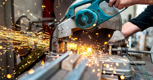 A worker's hands use a miter saw to cut a piece of metal. Lots of sparks are flying off the piece of metal.