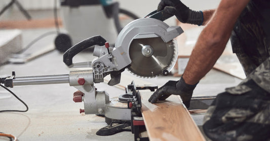 A professional using a circular saw to cut through a piece of laminate flooring in the middle of some construction.