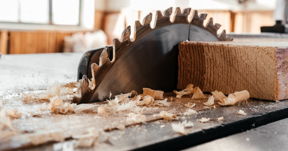 A closeup on a circular saw blade embedded in a table saw. There are multiple shavings of wood around the blade.