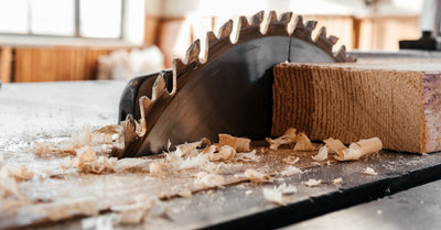 A closeup on a circular saw blade embedded in a table saw. There are multiple shavings of wood around the blade.