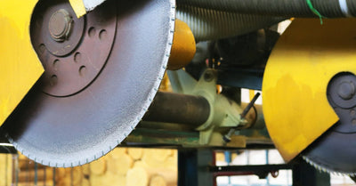 A pair of large circular saw blades in an industrial setting. The blades have thick, yellow safety guards around them.