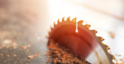 A singular, metallic, circular saw blade in a table saw. It is surrounded on all sides by saw dust particles.