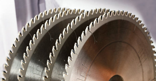 Four clean and sharp carbide-tipped saw blades stand next to each other in front of a grey metallic background.
